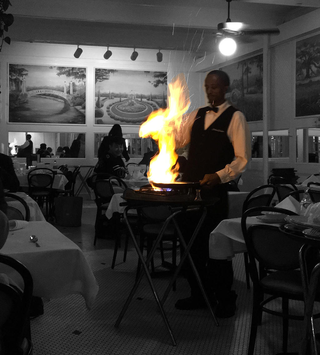 A waiter prepares Bananas Foster while Death stalks a fellow diner in the background